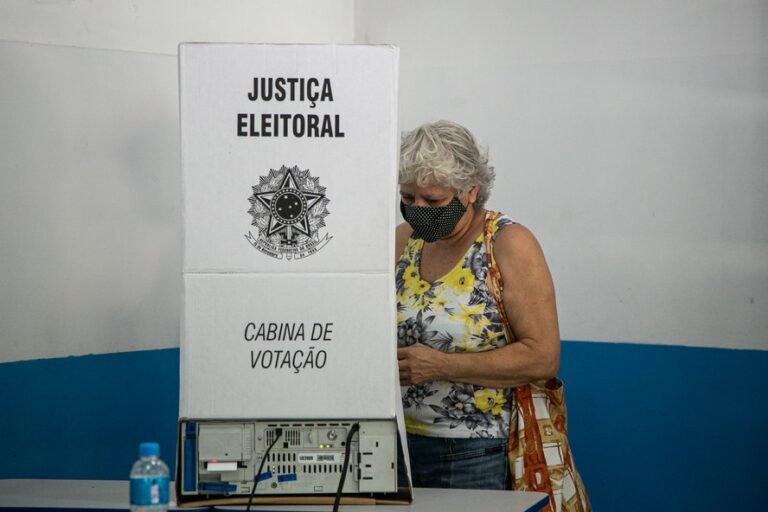Qual é a distância mínima para justificar o voto nas eleições 16 pessoas votando em uma cabine eleitoral